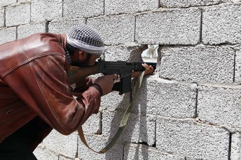 A Libyan rebel fighter fires his weapon through a hole in a wall during battle with pro-Gadhafi troops in the besieged city of Misrata.