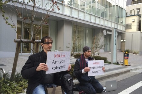 Two bitcoin traders hold protest signs as they conduct a sit-in in front of the office tower housing MtGox in Tokyo.