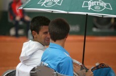 Novak Djokovic shares his umbrella with a ball boy during a French Open rain delay