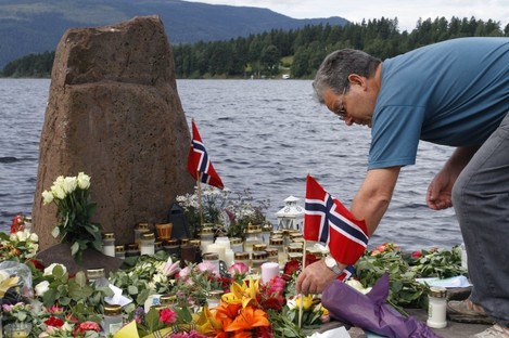 A man places a Norwegian flag between flowers in Utvika in front of Utoya island