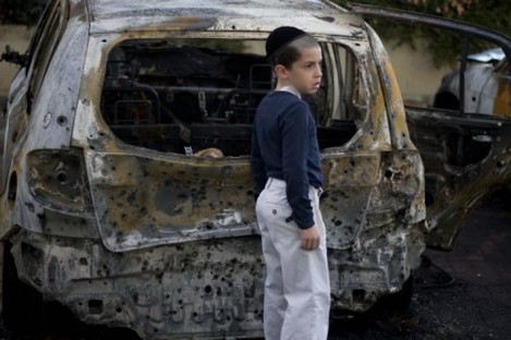 A boy stands next to a burned cars following Saturday night's rocket attacks from the Gaza Strip, in Ashdod, southern Israel, early Sunday, 30 October.
