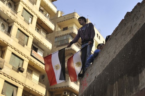 A young Egyptian man holds a national flag while standing on a rooftop between Tahrir Square and the Interior Ministry in Cairo