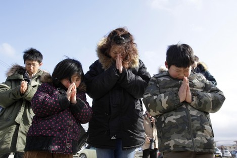 A family observes a moment of silence by the remains of a disaster centre in an area devastated by the tsunami