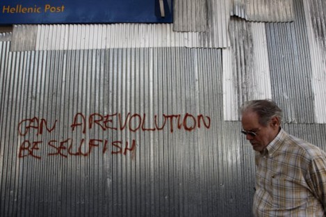 A Greek man walks past metal sheeting sprayed with a slogan in English reading "Can a revolution be selfish", that covers the facade of a post office branch in Syntagma Square, central Athens.