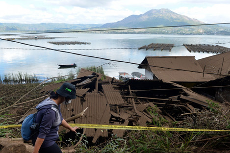 A woman walks past houses by Lake Batur which were damaged by an earthquake-triggered landslide in Bangli, on the island of Bali, Indonesia