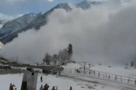 Snowboarders at the base of the mountain film the avalanche