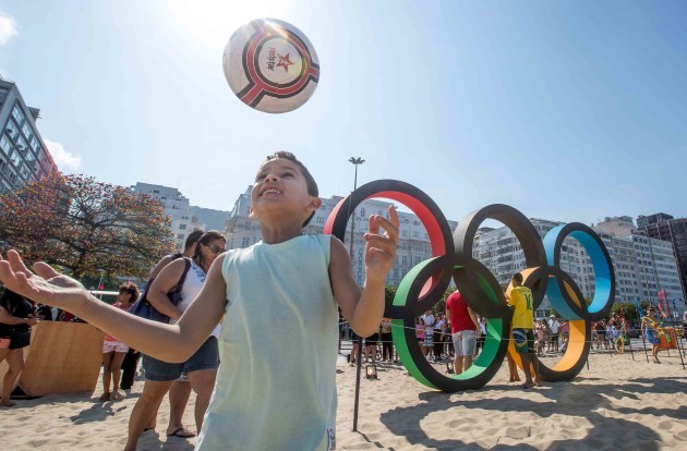 A young local boy plays football in front of the Olympic rings on Copacabana Beach