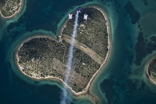 Marco Waltenspiel, Amy Chmelecki and Marco Fuerst fly with their wingsuits over the heart island