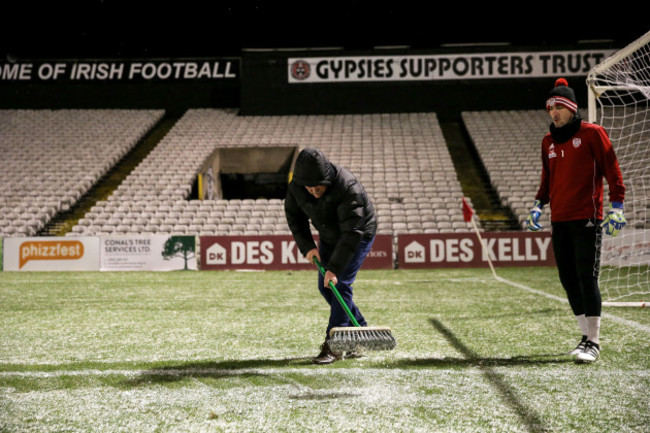 A member of the ground staff clears snow from the pitch