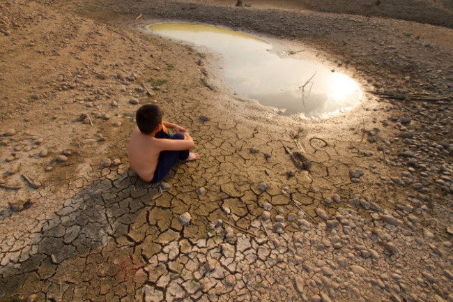 Water crisis, Child sit on cracked earth near drying water.