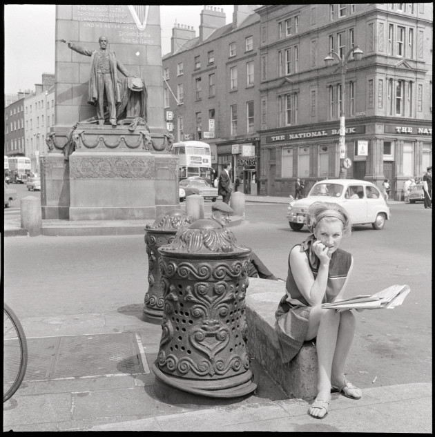 6. vtls000049027. - Woman sitting beside ornate ironwork bollards, Parnell Monument, O'Connell Street, Dublinjpg