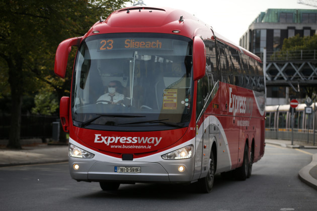 A single decker red coach with Expressway and Sligo written on the front. It is near Busáras as the Life Centre on Abbey Street is visible. A Luas and some trees are also visible in the background.
