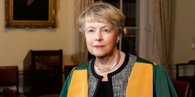 Dr Mary Canning wearing a green and yellow academic cape over a grey jacket and black top.