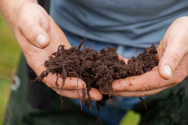 Carlow farmer Kevin O'Hanlon wearing a blue t-shirt standing in a field with dark, rich soil in his hands