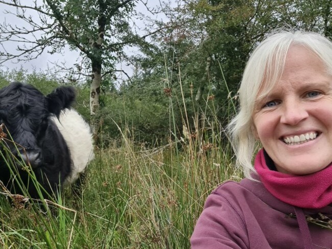 Farmer Nia O'Malley sitting on ground on her farm in Co Galway with her cows in the background