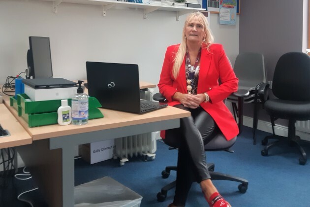 Mary Nevin wearing a red jacket sitting at her desk in front of her computer 