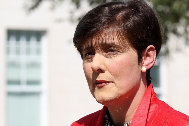 Minister Norma Foley - wearing a red jacket with a stone building in the background.