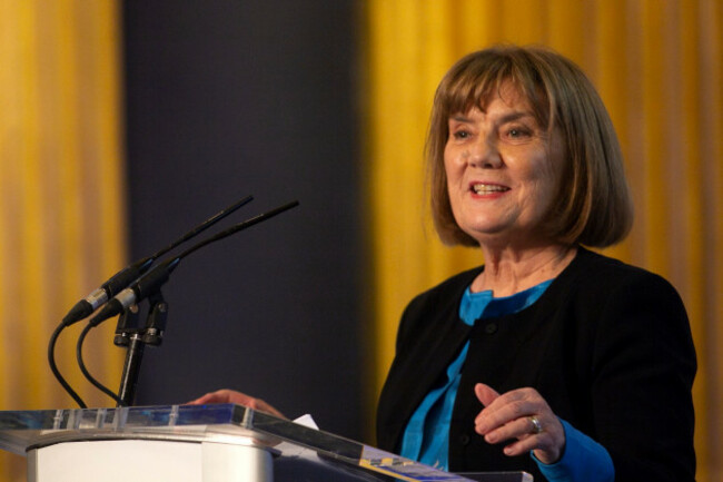 Dr Evelyn Mahon - wearing a blue top and black jacket - speaking at a podium with two microphones.