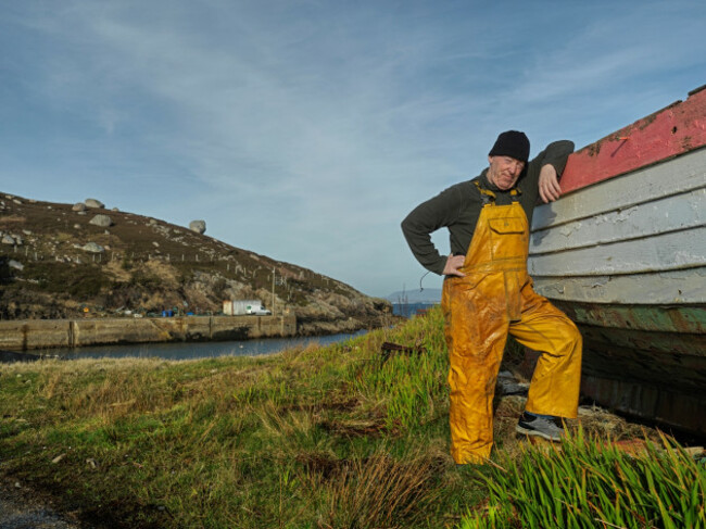 Jerry Early wearing yellow overalls leaning on a boat beside a harbour