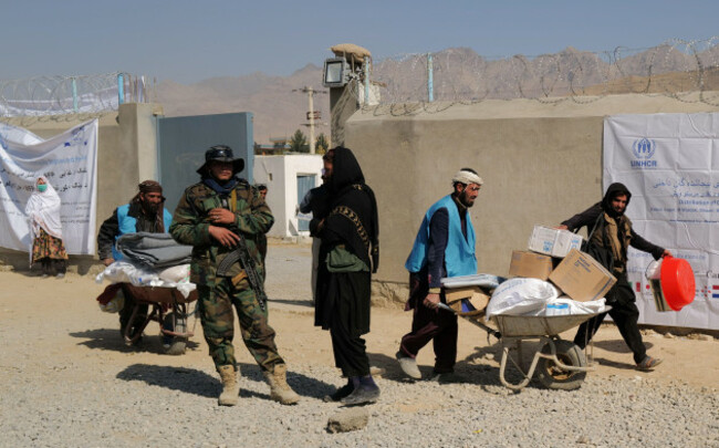 unhcr-workers-push-wheelbarrows-loaded-with-aid-supplies-for-displaced-afghan-families-as-a-taliban-fighter-secures-the-area-outside-the-distribution-center-on-the-outskirts-of-kabul-afghanistan-octo