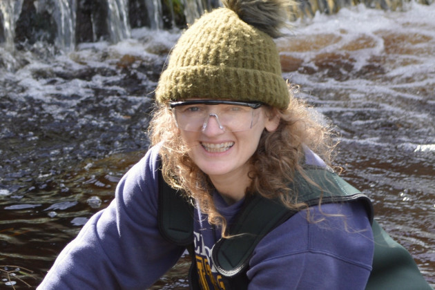 Trish Murphy wearing a bobble woolly hat and safety glass hunkered down while working in a river.