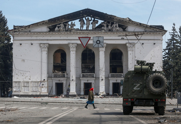 a-woman-walks-next-to-an-armoured-vehicle-of-pro-russian-troops-the-building-of-a-theatre-destroyed-in-the-course-of-ukraine-russia-conflict-in-the-southern-port-city-of-mariupol-ukraine-april-10-20