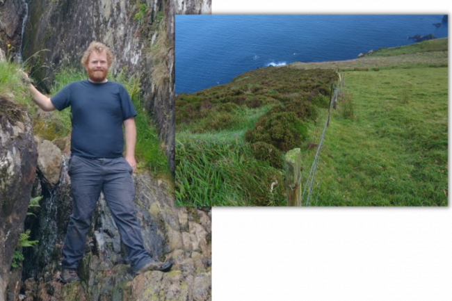 On the left is Dr Rory Hodd wearing a navy top and grey trousers standing on a rock face looking at the camera smiling. On the right is a slope down to the sea with two areas separated by a fence - with heather growing on the left of the fence but short grass on the right. 