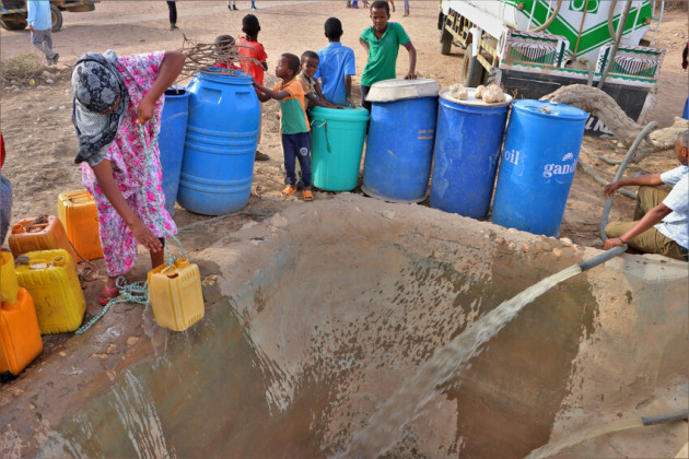Women collect water from well as it is being filled up by water truck