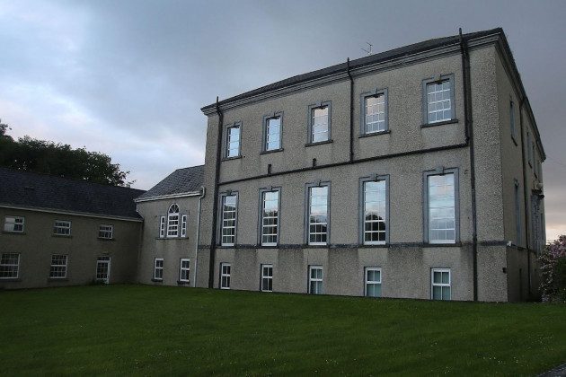 A large three story grey building with many windows and a lower two storey section attached. Both have grey slate roofs. 