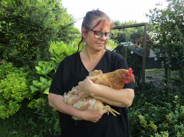 Caroline Rowley holding a chicken in her arms in front of a hedgerow
