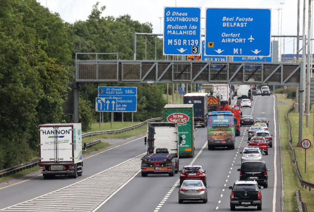 Cars and trucks on a section of M50 motorway with signs southbound to Malahide and to Belfast and the airport on the M1.
