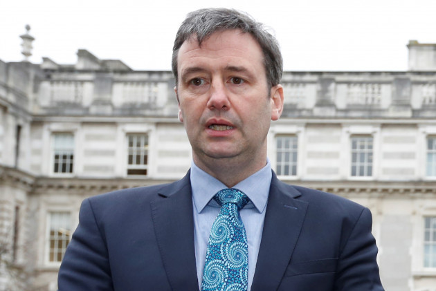 Michael D'Arcy standing outside wearing a light blue shirt, blue patterned tied and grey suit jacket.