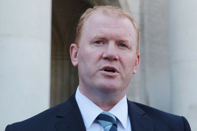 Paudie Coffey speaking outside - wearing a white shirt, striped tied and dark grey suit jacket.