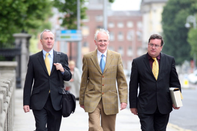 Dónal Geoghegan walking down a Dublin Street wearing a suit and shoulder bag. Walking beside him are then-Green Party chairman John Gormley wearing a tan suit, and talks negotiator Dan Boyle wearing a yellow tie and black suit. 