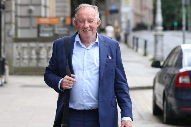 Tom Parlon - wearing a light blue shirt, navy jacket and shoulder bag - walking down a Dublin street. 