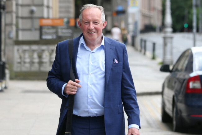 Tom Parlon - wearing a light blue shirt, navy jacket and shoulder bag - walking down a Dublin street. 