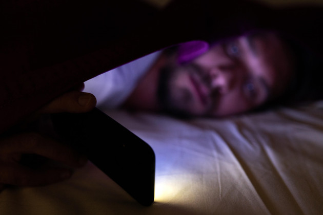 bearded-young-man-is-lying-in-bed-under-his-blanket-he-cannot-sleep-and-is-watching-something-on-his-mobile-phone