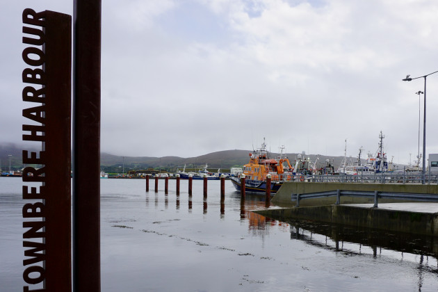 The Wild Atlantic Way Castletownbere Harbour sign is in the foreground with boats, including a lifeboat in the harbour behind.