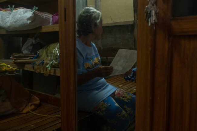 Older woman facing away to protect identity, sitting in a room behind a storage press, looking at a photograph.