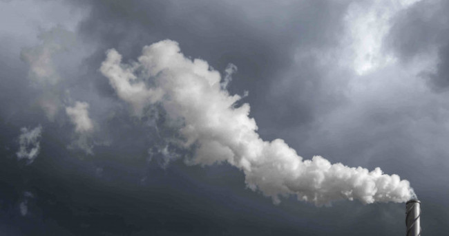 A chimney of a thermal power plant with smoke coming out with a deep blue sky