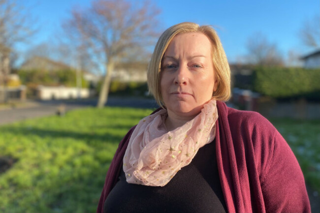 Thelma Carty wearing a pink scarf, black top and red cardigan standing in a green urban area.