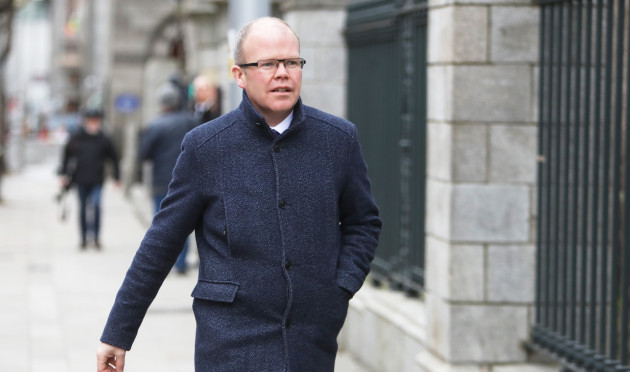Peadar Tóibín walking down a street in Dublin wearing a dark jacket and glasses.