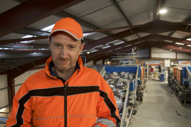 Mark Sheahan wearing and orange hi-vis jacket and cap in front of machines in the Limerick plant.