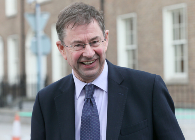 Éamon Ó Cuív smiling in a dark blue suit, light blue tie and glassed