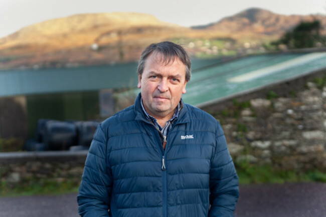 John Walsh in a navy jacket with the sea and mountains in the background