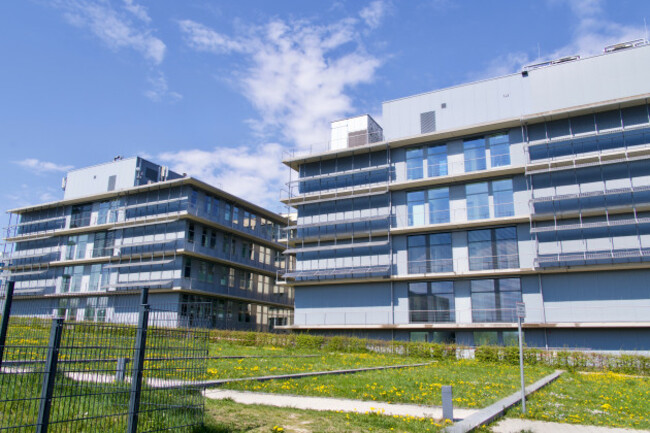 Two industrial buildings with four stories with windows surrounded by grass.