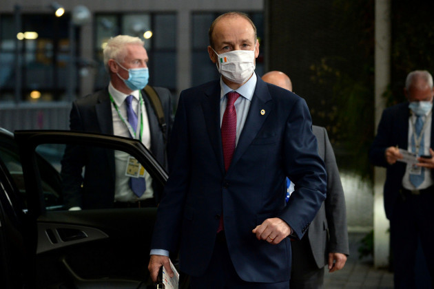 Micheál Martin wearing a suit and face mask standing beside the open door of a car. 