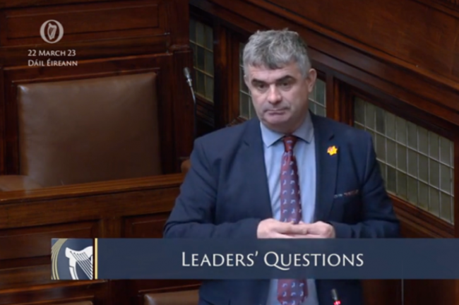 Richard O'Donoghue wearing a suit and tie speaking in the Dáil chamber. Dáil Éireann 22 Mar 2022 and Leaders Questions are written on the screen.