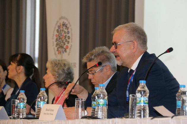 Harald Hartvig Jepsen sitting at a conference table with other delegates in a dark suit and glasses speaking into the microphone