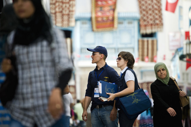  Two EU observers in blue tops and sunglasses looking around in a busy pedestrian street in Tunisia. 